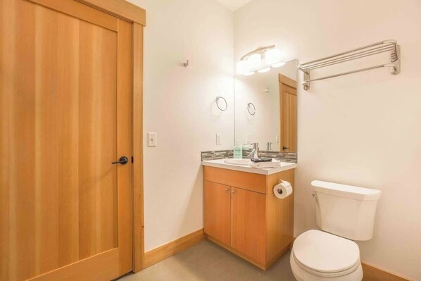 Un baño con puerta de madera, un lavabo con espejo, un inodoro y un perchero para toallas.