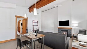 A modern living room with a fireplace, a sofa, a dining table with chairs, and a television mounted on the wall. - Walk to Village-Fireplace-Festhalle Section (Leavenworth)