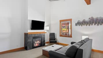 Una sala de estar con chimenea, un televisor de pantalla plana montado arriba, un sofá gris y un ventanal con vistas a edificios.