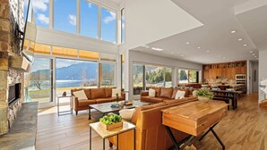 A spacious living area with a fireplace, large windows, and a kitchen with wooden cabinets. - Private beach with panoramic lake views (Entiat)