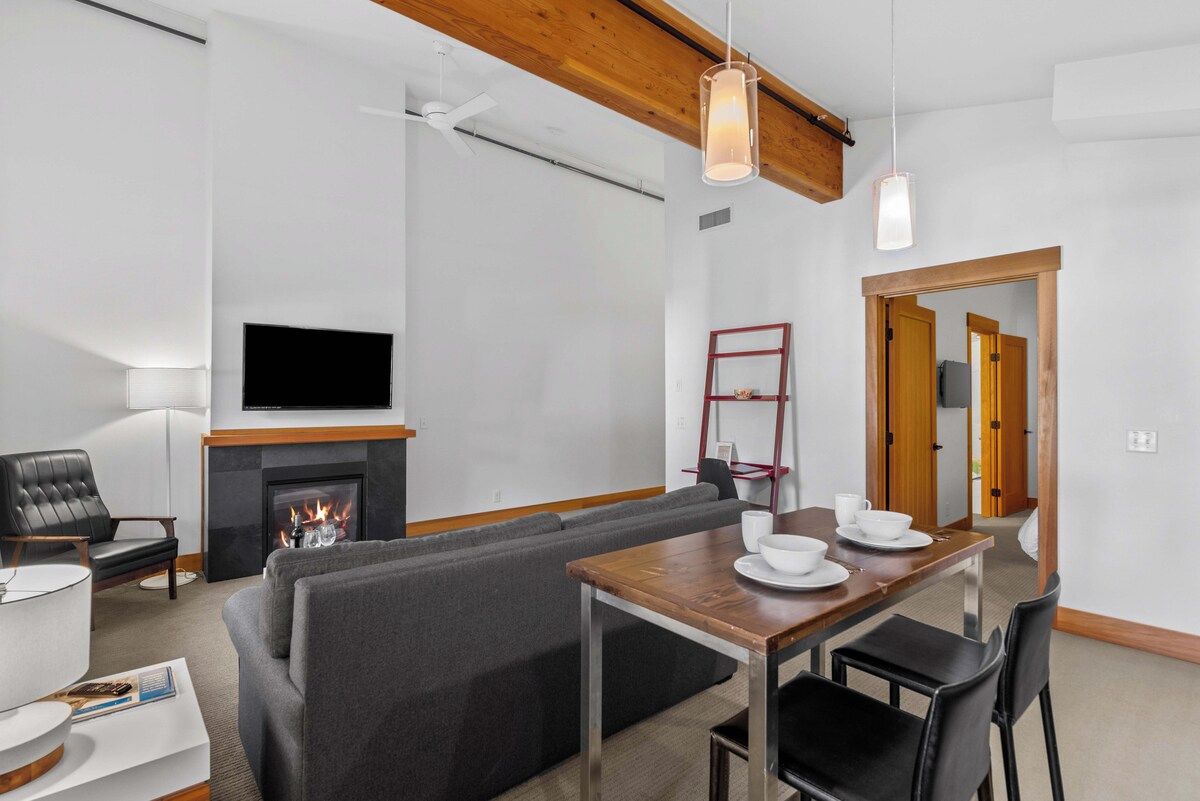 Een moderne woonkamer met een open haard, een eettafel en een bank.