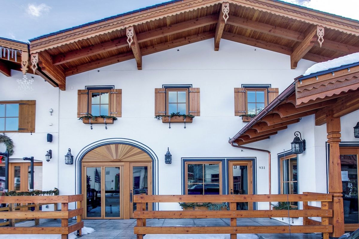 Una cabaña tradicional con vigas de madera, ventanas amplias y un techo cubierto de nieve.