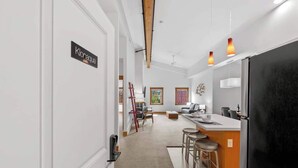 Eine moderne Küche mit einem schwarzen Kühlschrank, einem Essbereich mit Hockern und einem Wohnbereich mit einer Couch und einem Gemälde.