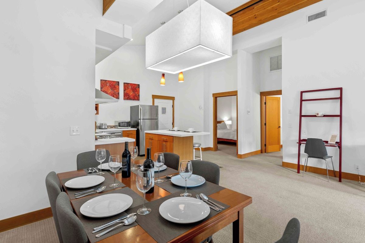 Een moderne eethoek met een houten tafel voor vier personen, een keuken op de achtergrond en een rode metalen schapunit.
