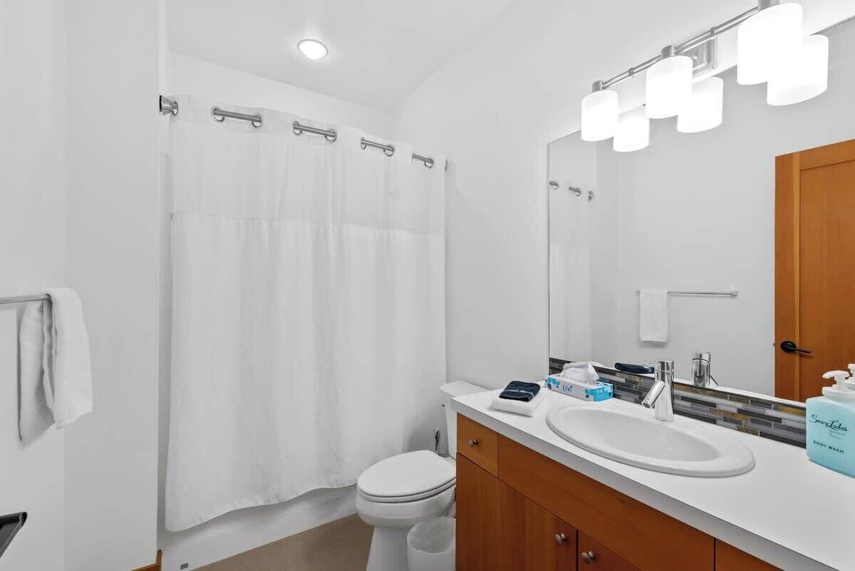 A modern bathroom with a white toilet, a shower curtain, a vanity with a sink, a mirror, and a towel rack.