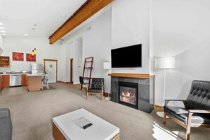 A modern living room with a fireplace, a flat-screen TV, and a dining area with a kitchen in the background. - As twilight descends over the Cascade Mountains, your private balcony at Front S (Leavenworth)