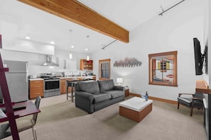 A modern kitchen with a built-in oven, a dining area with a table and chairs, a gray sofa, and a coffee table. - As twilight descends over the Cascade Mountains, your private balcony at Front S (Leavenworth)