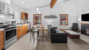 Eine moderne Küche mit Edelstahlgeräten, ein Essbereich mit Tisch und Stühlen, ein schwarzes Sofa und ein Kamin.