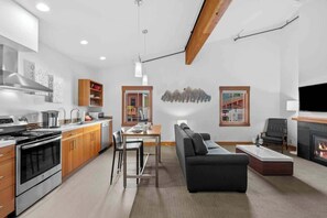 Eine moderne Küche mit Edelstahlgeräten, ein Essbereich mit Tisch und Stühlen, ein schwarzes Sofa und ein Kamin.