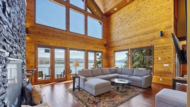 Ein geräumiges Wohnzimmer mit einer großen Eckcouch, einem Couchtisch und Blick auf einen See durch große Fenster.