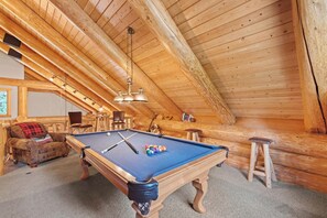 Une table de billard dans une pièce en bois, dotée d’un plafond en pente et d’un coin salon accueillant.