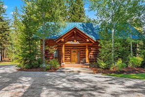 Une cabane en rondins avec un porche à l’avant, entourée d’arbres.