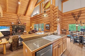 L’intérieur d’une cabane en rondins présente une cheminée en pierre, une table à manger en bois et un coin cuisine doté de plans de travail en granit.