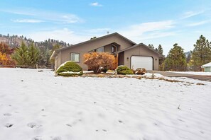 A single-story house with a garage, surrounded by snow-covered ground and a few trees. - As the sun dips behind the Cascade Mountains, the warm glow of the river-rock ga (Leavenworth)