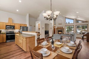 A spacious kitchen with wooden cabinets, a dining area set for four, and a fireplace. - As the sun dips behind the Cascade Mountains, the warm glow of the river-rock ga (Leavenworth)