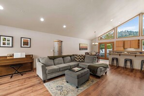 A modern living room with a sectional sofa, a piano, and a dining area. - As the sun dips behind the Cascade Mountains, the warm glow of the river-rock ga (Leavenworth)
