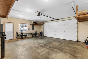 A garage with a white garage door, a table with chairs, and a ceiling fan. - As the sun dips behind the Cascade Mountains, the warm glow of the river-rock ga (Leavenworth)
