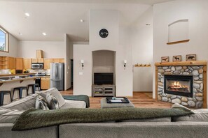 A modern living room with a fireplace, a kitchen area with appliances, and a seating area with a sofa. - As the sun dips behind the Cascade Mountains, the warm glow of the river-rock ga (Leavenworth)