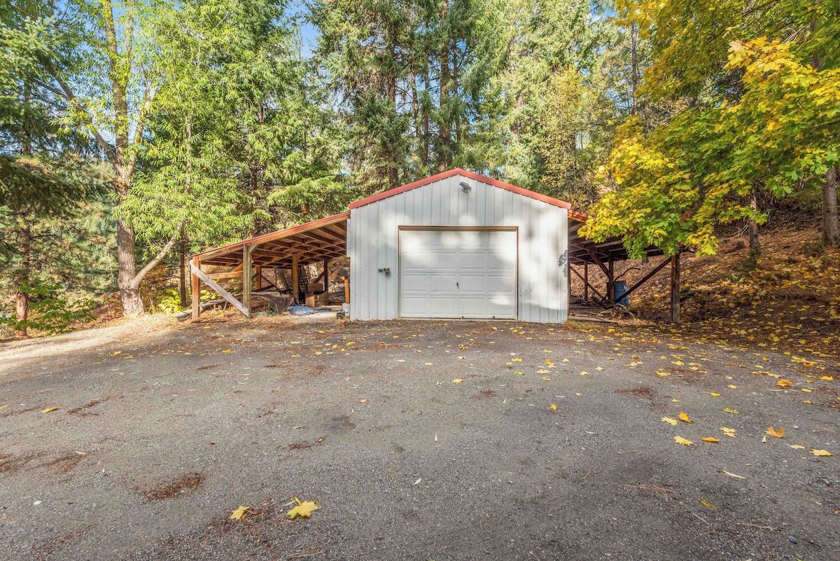 A single-story building with a garage, surrounded by trees and a gravel driveway.