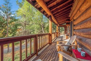 A wooden deck with a railing, wooden chairs, and a bench.