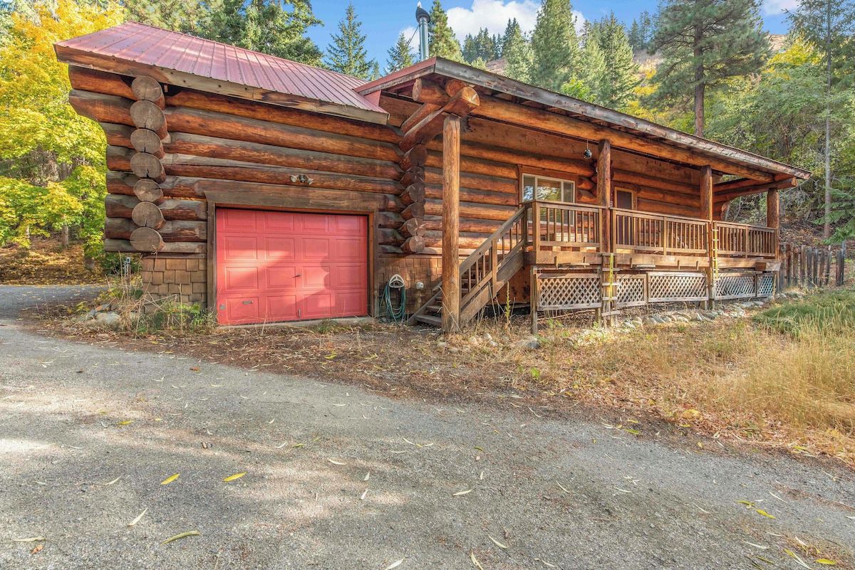 A log cabin with a red garage door, a porch with a railing, and a staircase leading to the entrance.