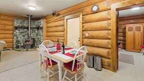 Ein gemütliches Blockhaus-Interieur mit Kamin aus Stein, Holzwänden, einem Esstisch für vier Personen und einer Wanduhr.