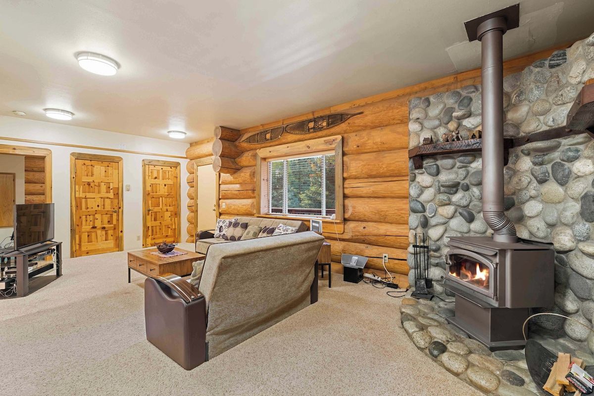 A log cabin interior with a stone fireplace, wooden walls, a sofa, and a television.
