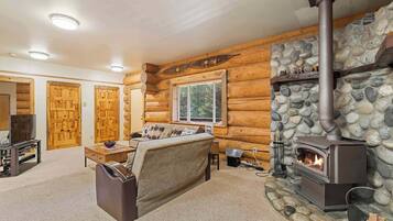 A log cabin interior with a stone fireplace, wooden walls, a sofa, and a television.