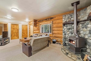 Ein rustikales Blockhaus mit Kamin aus Stein, Holzwänden, einer Couch und einem Fernseher.