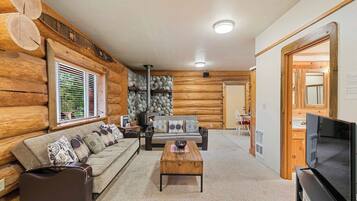 A log cabin interior with a sofa, coffee table, fireplace, and television.