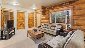 Ein Holzblockhaus-Interieur mit einer Couch, einem Fernseher und Holztüren.