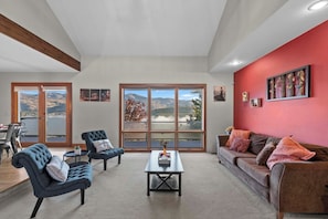 A modern living room with a large window, a red accent wall, and a view of the outdoors. - As the Chelan Valley sky transitions into twilight, take your place in the steam (Manson)