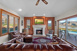 A living room with a fireplace, leather sofas, a television, and large windows with a view of a mountainous landscape. - As the Chelan Valley sky transitions into twilight, take your place in the steam (Manson)