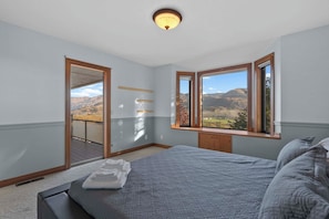 A bedroom with a large bed, a view of mountains, and a balcony. - As the Chelan Valley sky transitions into twilight, take your place in the steam (Manson)