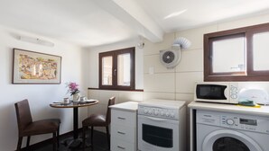 Eine kompakte Küche mit Mikrowelle, Backofen und Waschmaschine. Ein kleiner Esstisch mit Stühlen und ein gerahmtes Bild an der Wand.