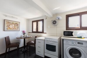 Una cocina compacta equipada con microondas, horno y lavadora. Hay una pequeña mesa de comedor con sillas y un cuadro en la pared.