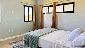 A bedroom with a bed, a window with curtains, an air conditioning unit, and a rug. - Coastal at Haven+ (St.kitts)