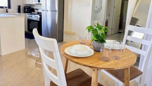 A modern kitchen with white cabinets, stainless steel appliances, and a wooden dining table with chairs. - Coastal at Haven+ (St.kitts)
