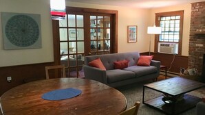 Un salon chaleureux avec une table ronde en bois, un canapé gris agrémenté de coussins rouges et une table basse moderne.