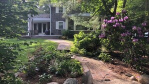 Une maison avec un chemin de briques menant à un porche, entourée d’une végétation luxuriante et de plantes en fleurs.