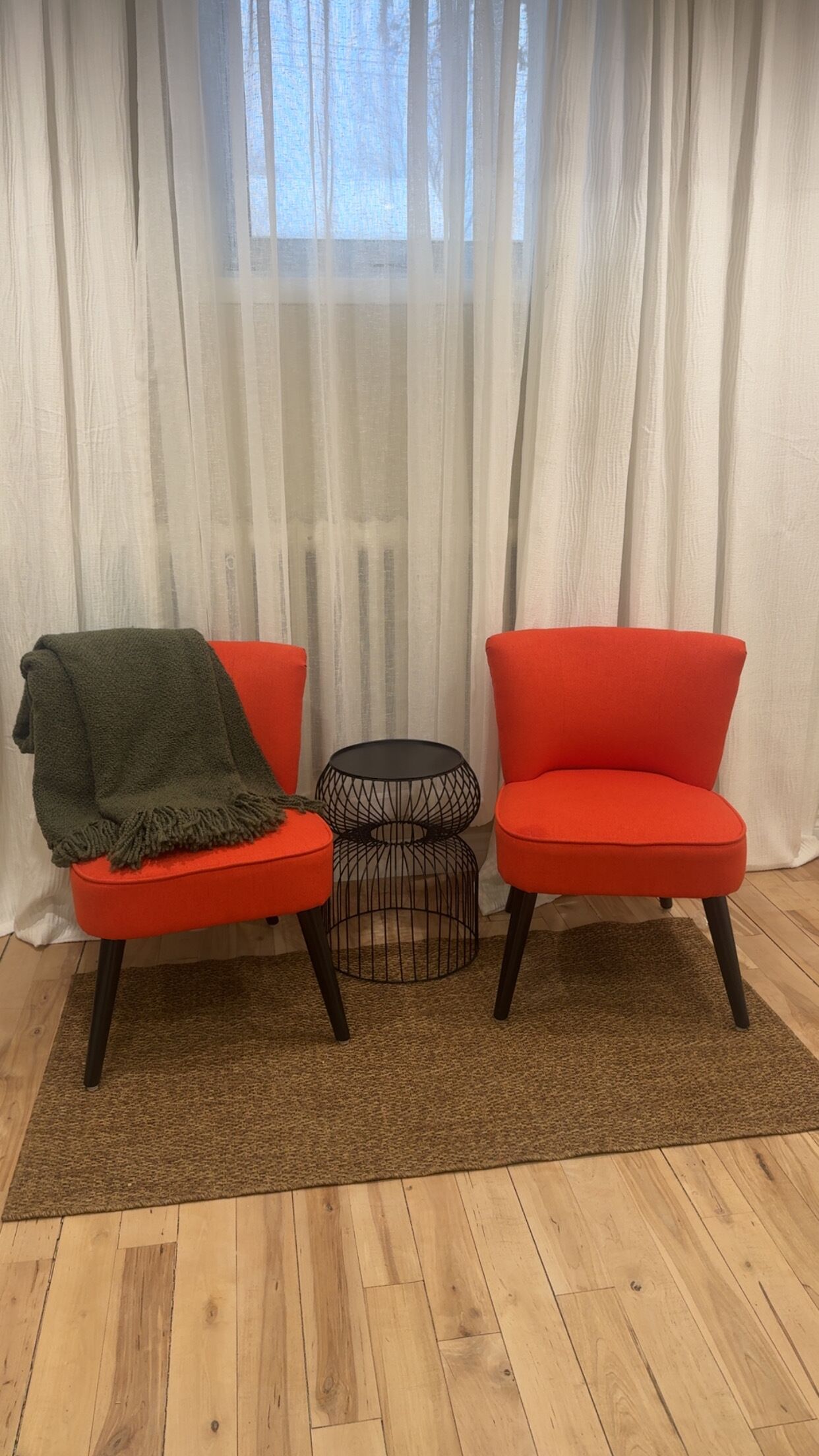 A room with two red chairs, a small black table, and a brown rug on a wooden floor.