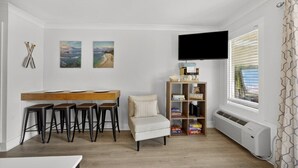 Un salon moderne avec une table à manger en bois, des tabourets de bar, un canapé, une bibliothèque et un téléviseur à écran plat.