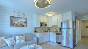 Une cuisine moderne avec des meubles blancs, des appareils en acier inoxydable et une décoration murale sur le thème de la plage.