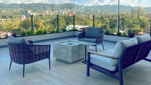 Une terrasse sur le toit, aménagée avec du mobilier d’extérieur, un foyer et offrant une vue sur la ville.