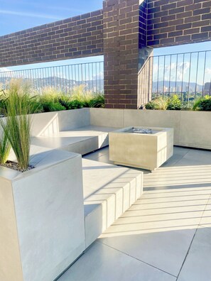 Una terraza en la azotea con diseño moderno, con macetas de concreto con plantas, un área de estar y vistas de la ciudad.