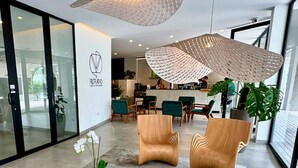 Un espace d’accueil moderne agrémenté d’un logo, de deux fauteuils en bois, d’une table basse et d’un grand luminaire suspendu.