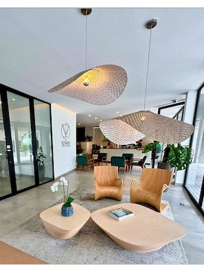 A modern reception area with a logo, two wooden chairs, a coffee table, and a large hanging light fixture. - Modern Apt z:10+jacuzzi+laundry+AC+GYM@GTCity (Ciudad de Guatemala)