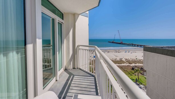 Een balkon met uitzicht op een strand, een pier en een heldere lucht.