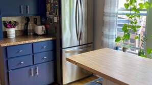 Une cuisine moderne avec des meubles de couleur bleu foncé, un réfrigérateur en acier inoxydable, un plan de travail en bois et une fenêtre offrant une belle vue.