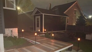 Une maison dotée d’une terrasse en bois, d’un petit abri de jardin et d’un espace jardin agrémenté d’un sentier.